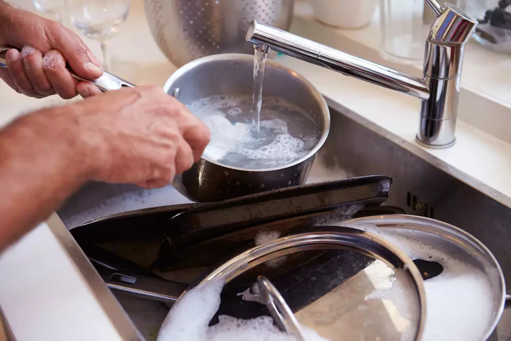 Man Washing Stainless Steel Pans In Sink